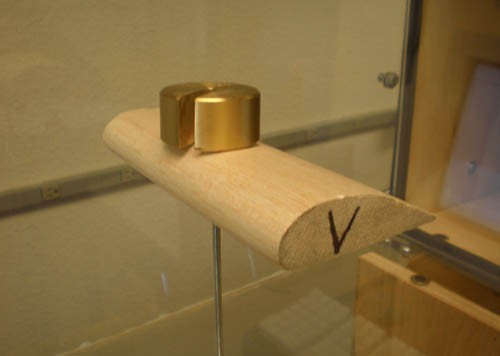 Two small weights are placed on a wooden block that is cut into the shape of an airplane wing