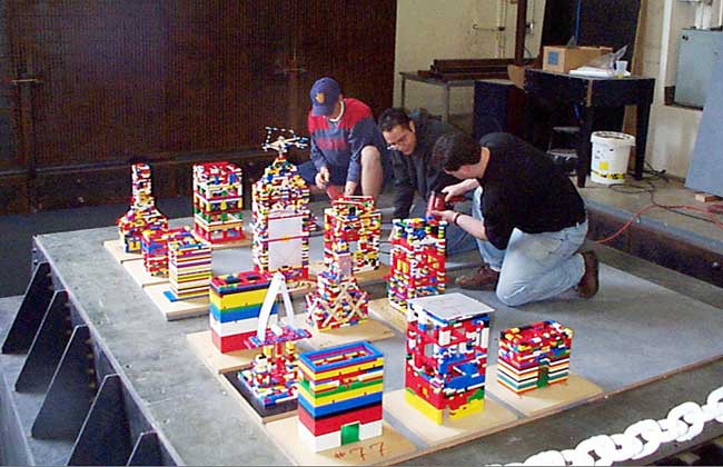 Three men use LEGOs to construct buildings of various shapes and sizes