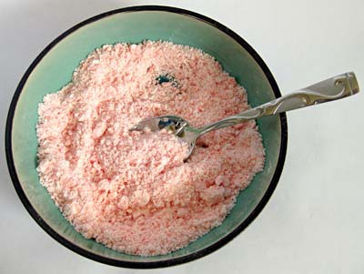A crumbling pink powder is mixed in a bowl with a spoon