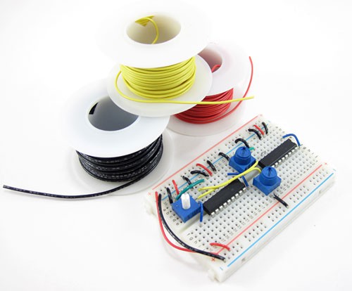 A wired breadboard next to three spools of yellow, red and black hookup wire
