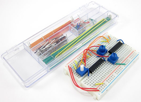 A wired breadboard next to a container filled with flexible jumper wires of different sizes
