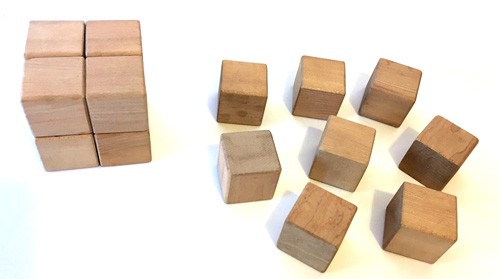 Eight small cubes form a larger cube next to eight small cubes spread out on a table