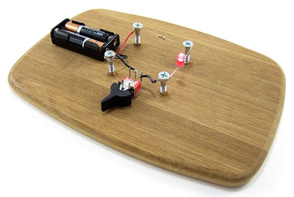 A switch, battery pack, resistor and LED are attached to a wooden board with screws