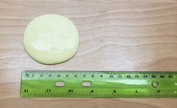 A circular puddle of green slime next to a ruler
