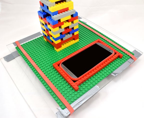 A smartphone is placed on a plexiglass sheet next to a building made of LEGOs
